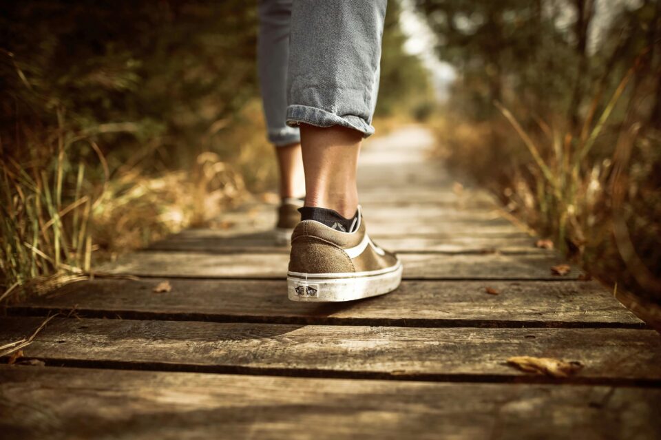 Lungo un sentiero nella natura, persona cammina a piedi (dettaglio scarpe da ginnastica chiare e jeans)